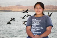 Image of girl with hands crossed in front of her. Edited background behind her of a body of water with geese flying.
