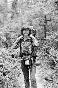 Audrey Klein holding backpack, walking in the forest.