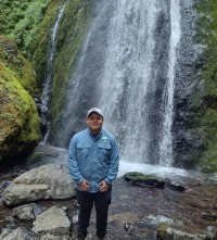 Photo of Alonso Castillo standing next to a waterfall smiling.